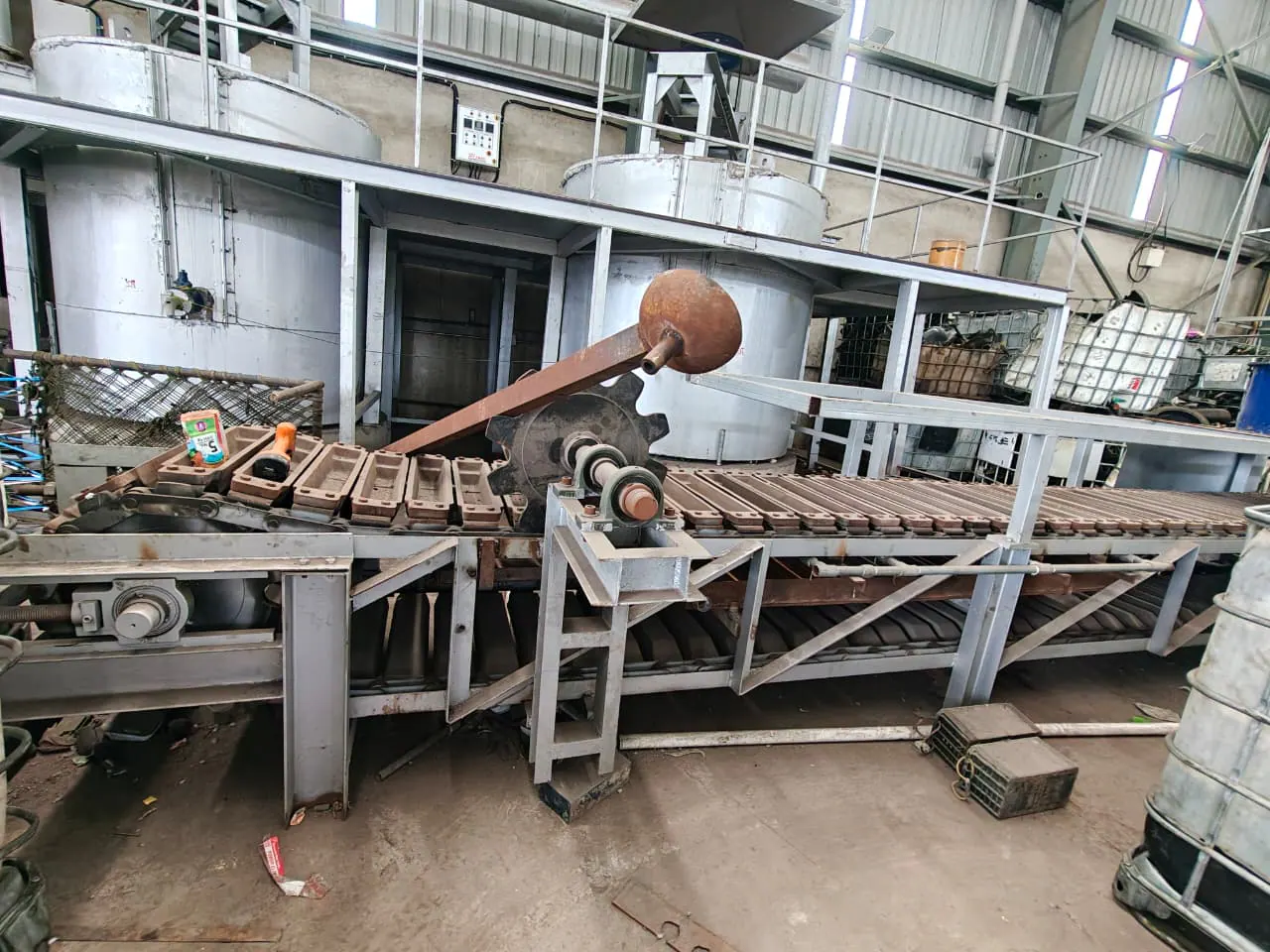 Driven chain conveyor carrying repeated metal moulds with its shaft and counterweighted mechanism visible