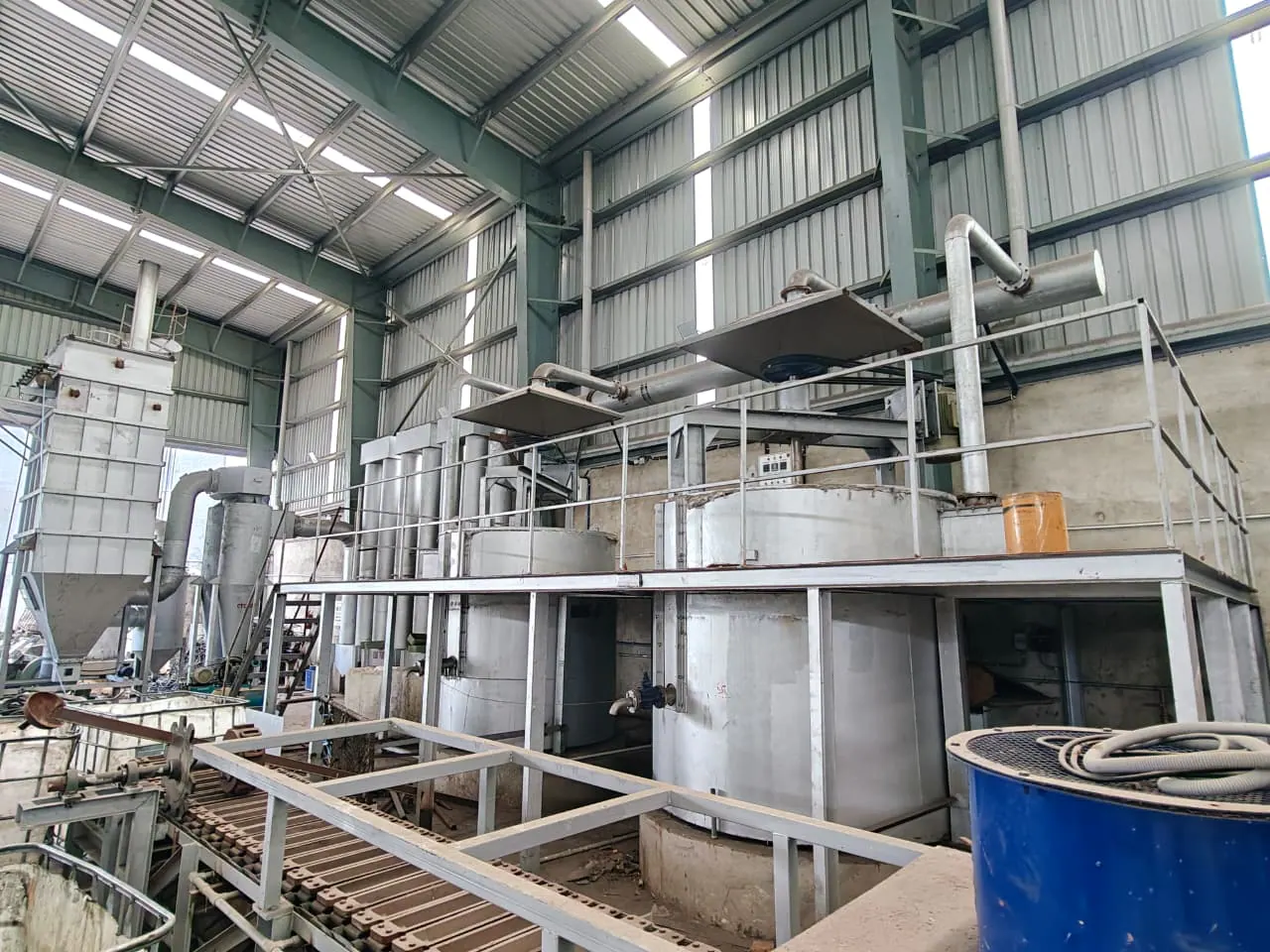 Two process vessels beneath extraction hoods with a foreground conveyor and pollution-control equipment